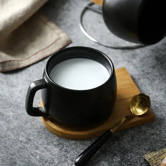 Black Ceramic Mug with milk inside next to a golden spoon on a wooden tray 