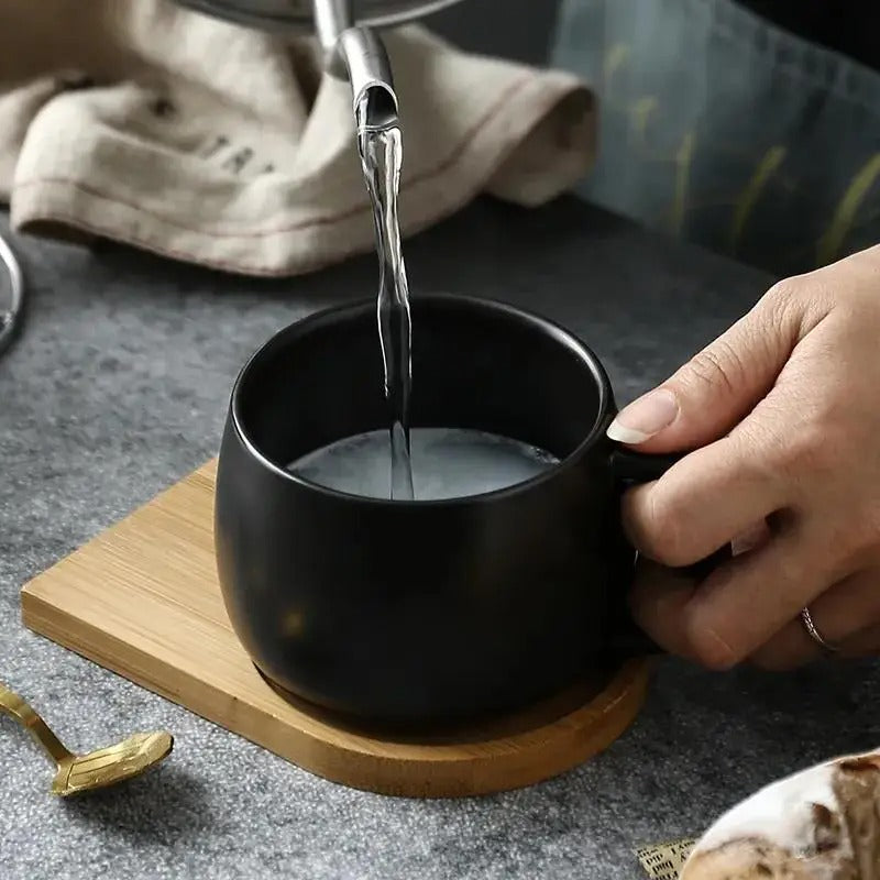 Person pouring hot water into a Black Ceramic Mug on a wooden tray 